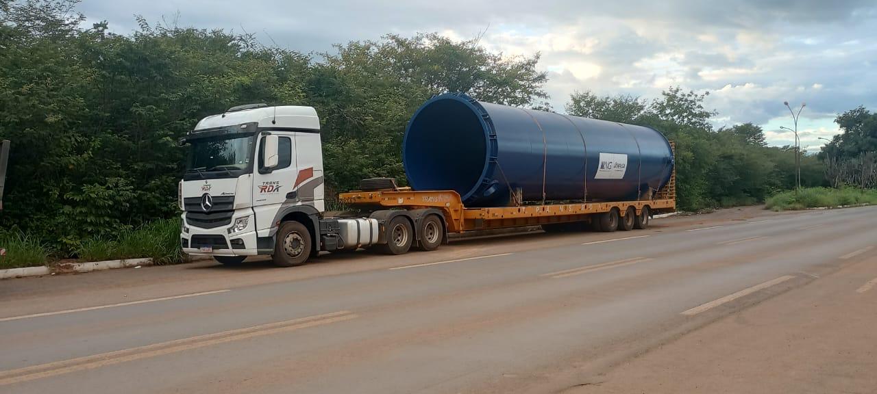 Caminhão RDA transportando equipamento cilíndrico em rota de projeto
